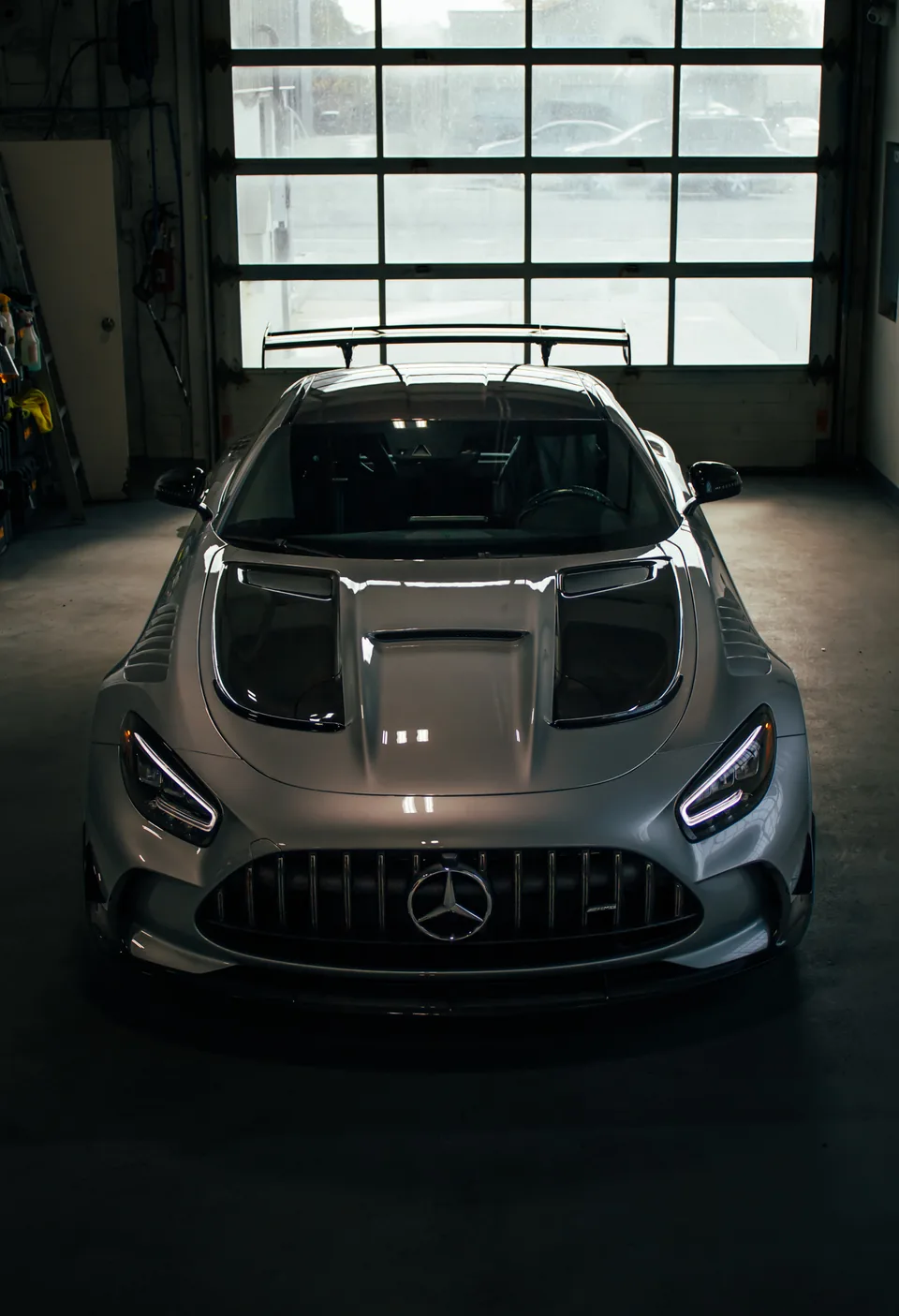 A silver Mercedes-AMG Black Series head-on in a garage, daylight flooding through the bay door behind it.