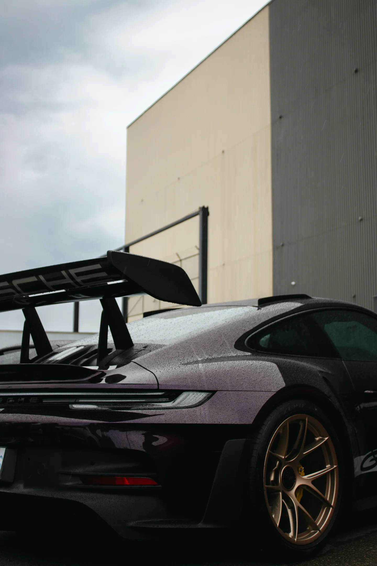 The rear wing of a purple Porsche 911 GT3 RS against a blank concrete wall at the Autostrada x Toybox meet.