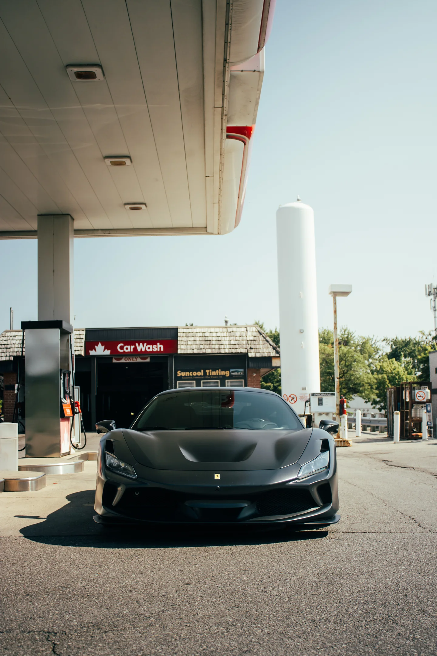 A black Ferrari F8 Tributo head-on at the pumps, canopy light on the roofline.