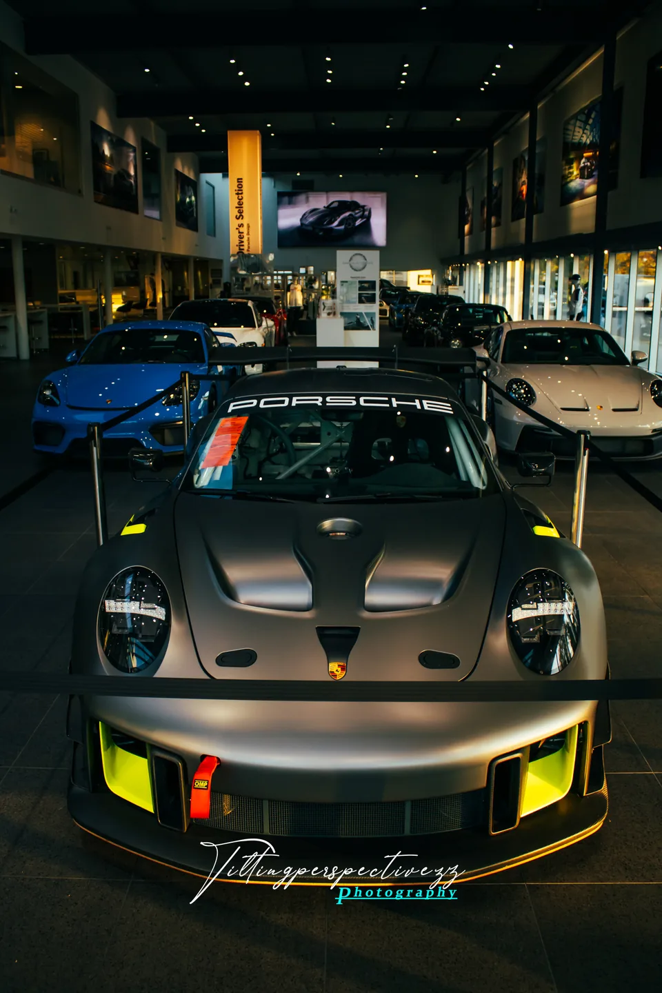 A Porsche GT2 RS Clubsport head-on in a showroom, yellow accents lit under the lights.