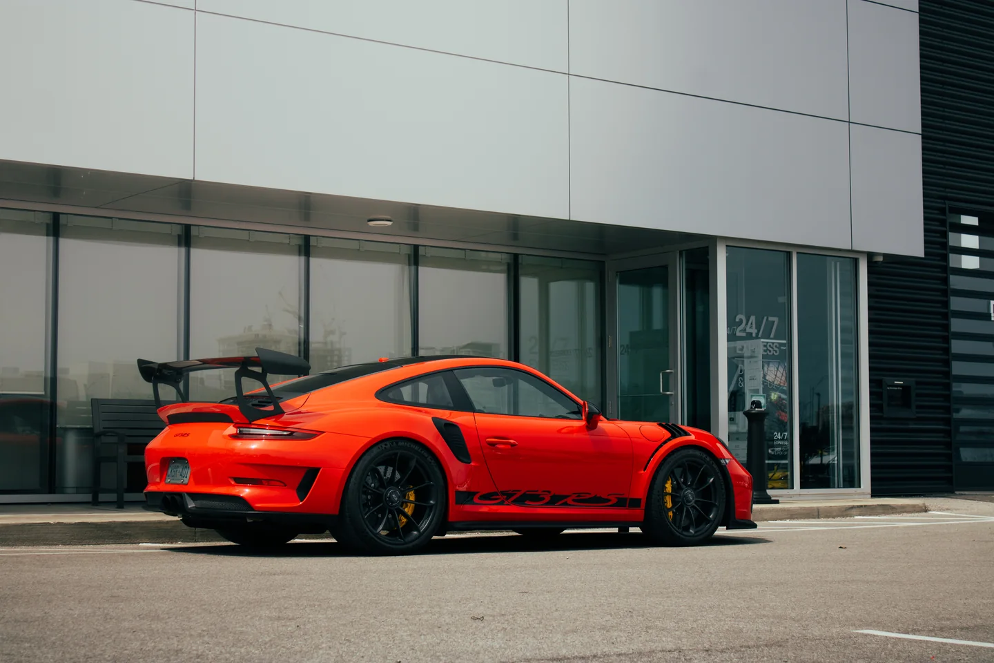 An orange Porsche 911 GT3 RS in profile on the forecourt of a Porsche dealership.