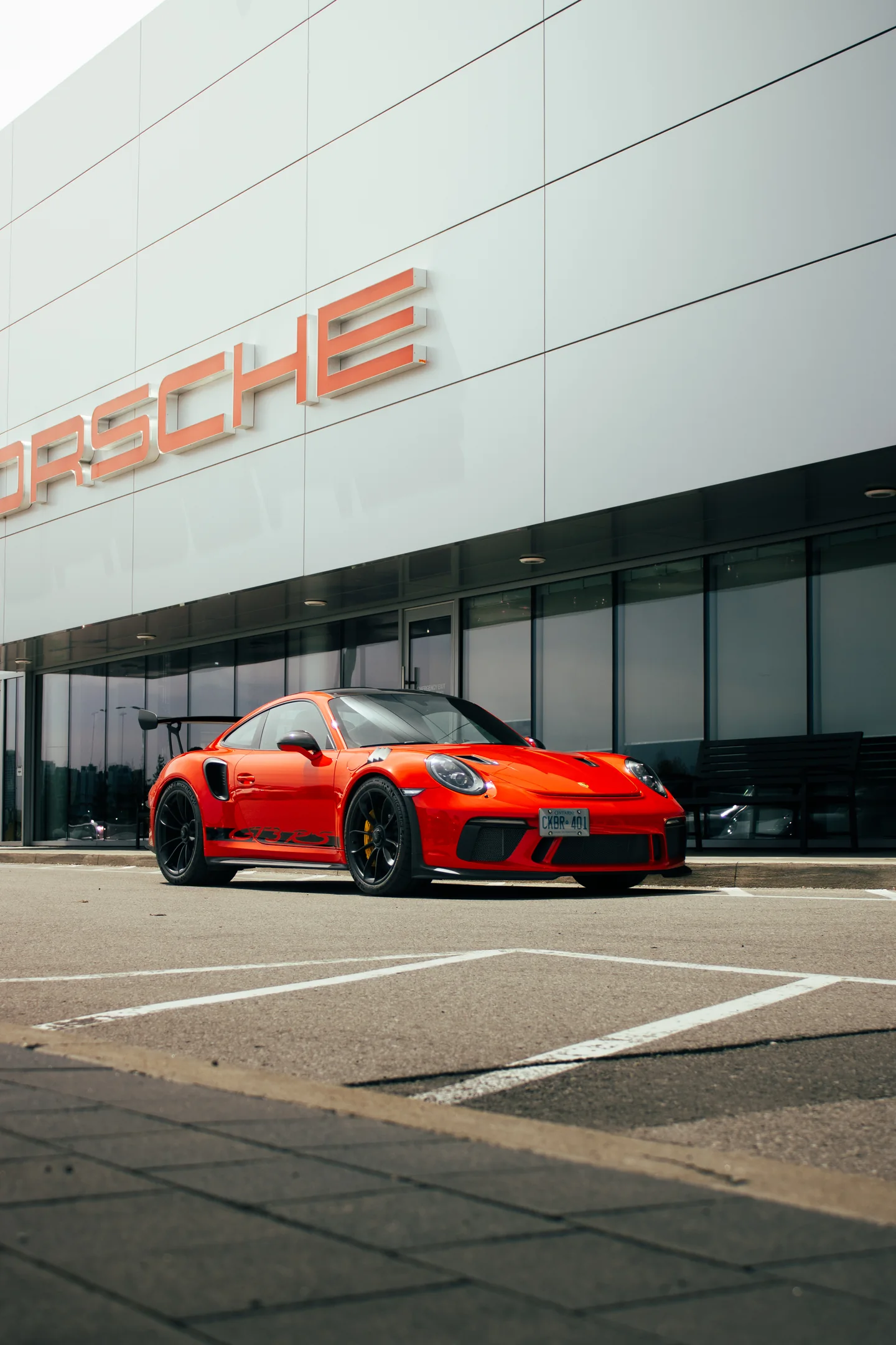 Ground-level view of an orange Porsche 911 GT3 RS beneath the Porsche sign.