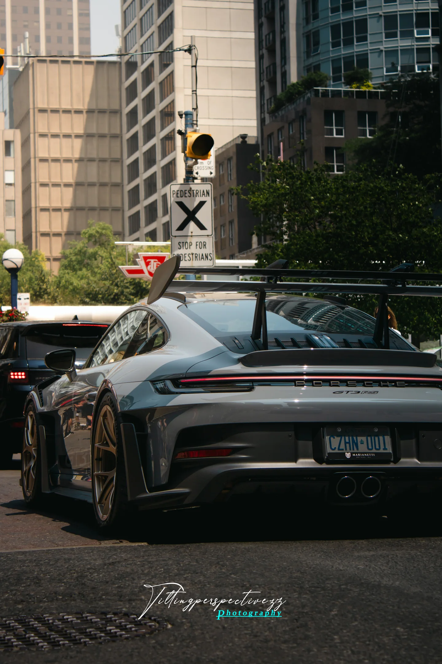 A grey Porsche 911 GT3 RS waiting at a downtown Toronto intersection, towers and traffic signals above it.