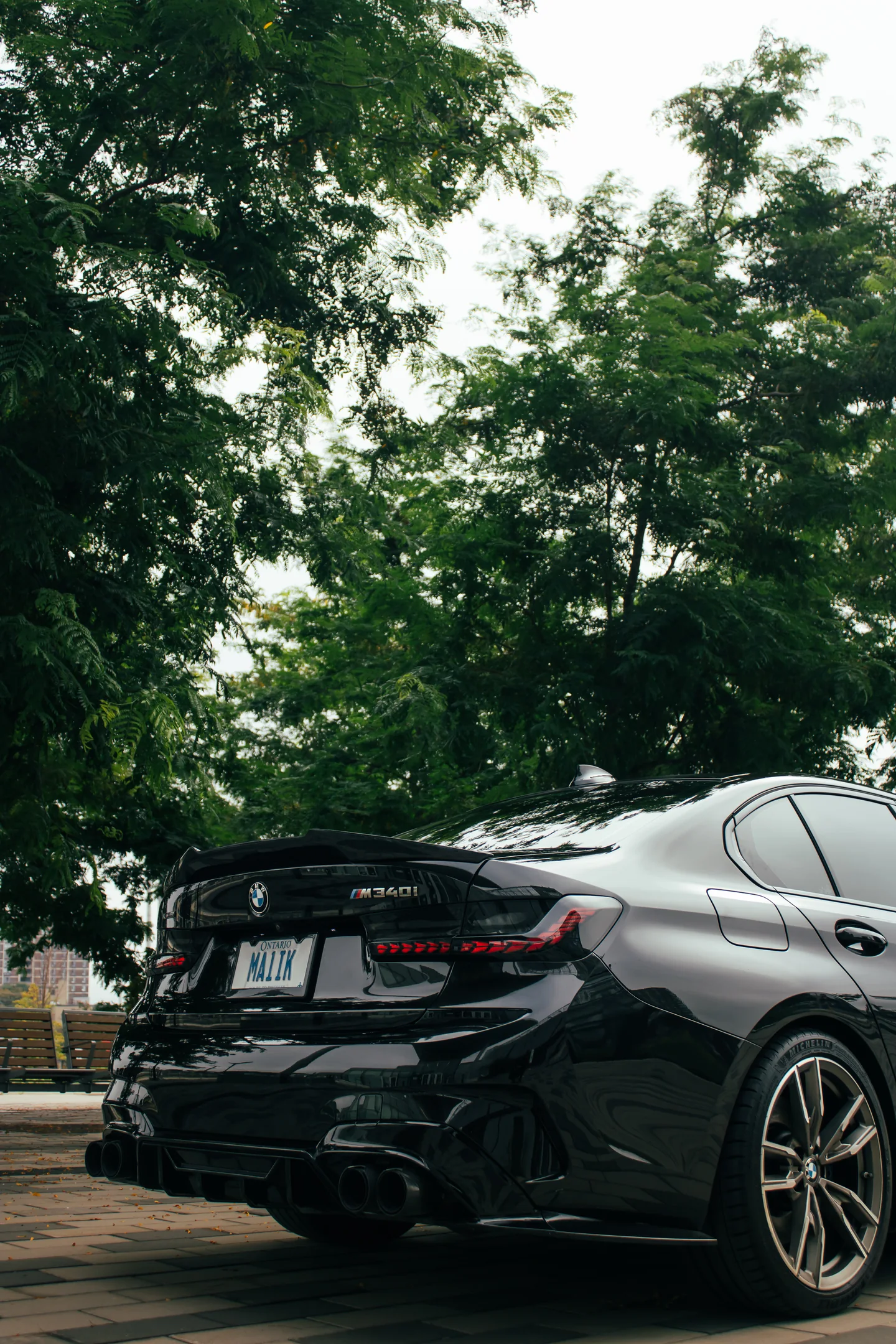 Rear three-quarter of a BMW M340i under a heavy summer canopy.