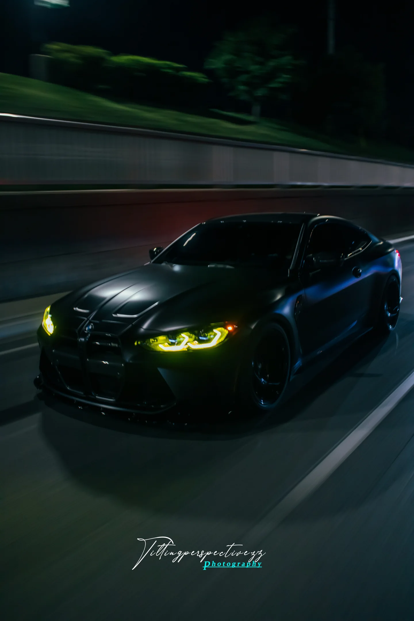 A BMW M4 at night with its headlights burning yellow, the background pulled into motion blur.