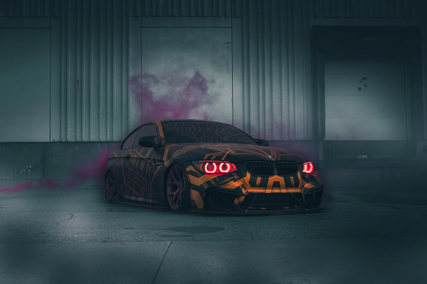A liveried BMW in a garage with pink smoke drifting around it, headlights lit.