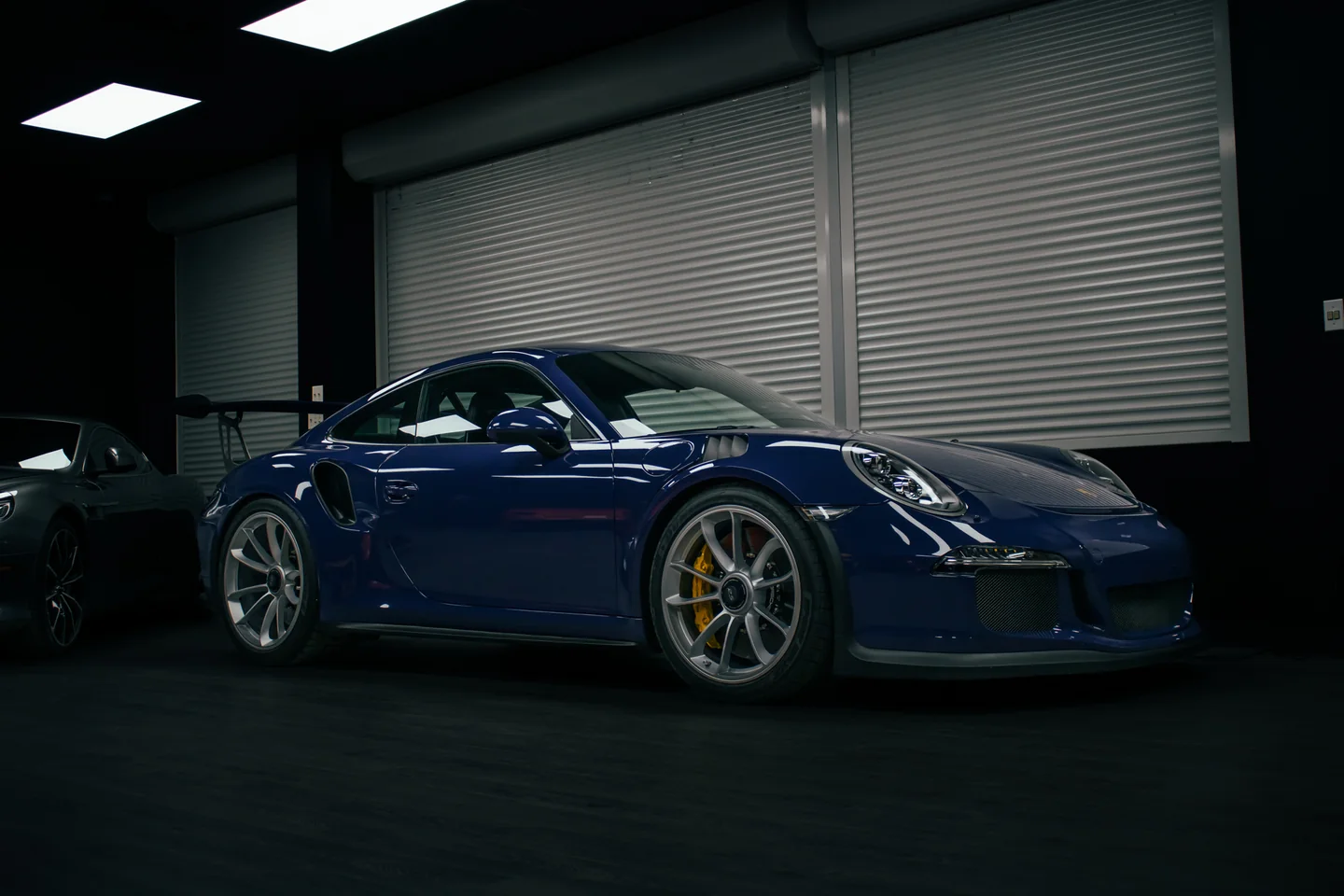 A blue Porsche 911 alone in a dark showroom, the only light falling from above.