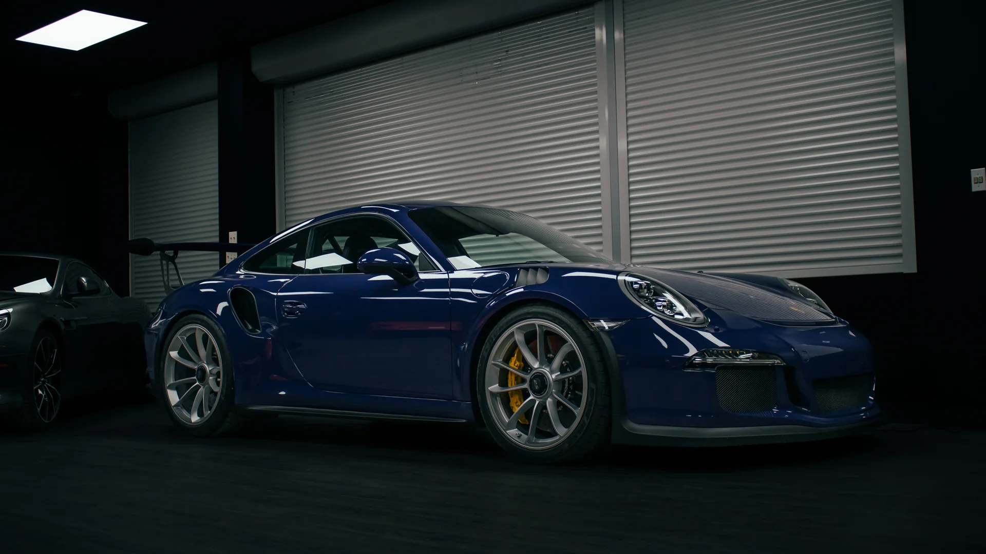 A blue Porsche 911 alone in a dark showroom, the only light falling from above.