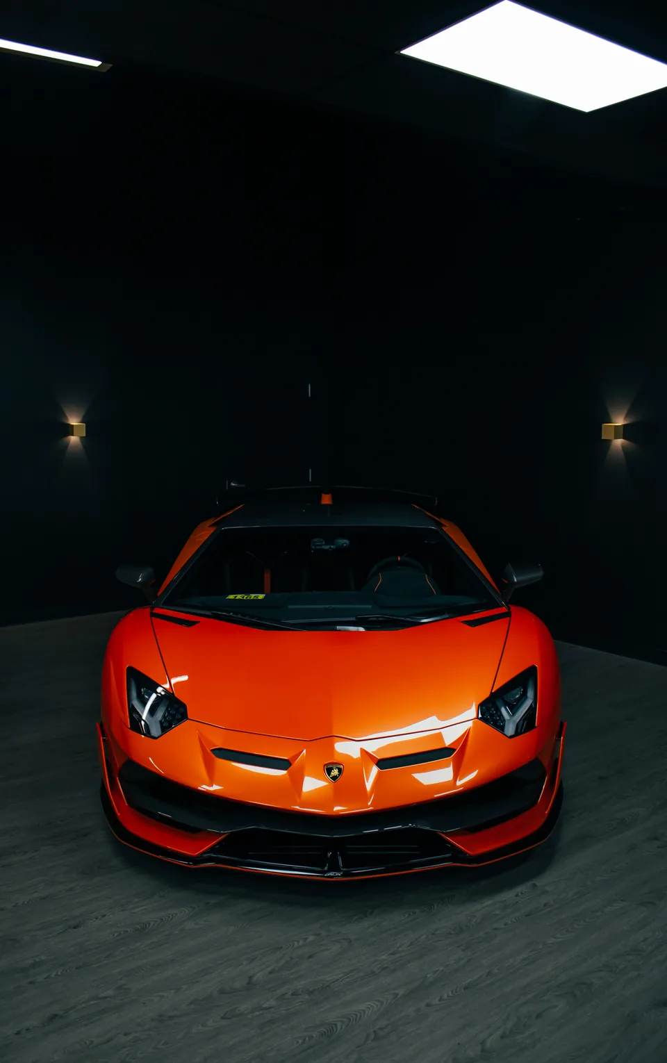 An orange Lamborghini head-on in a near-black garage, ceiling lights burning above it.