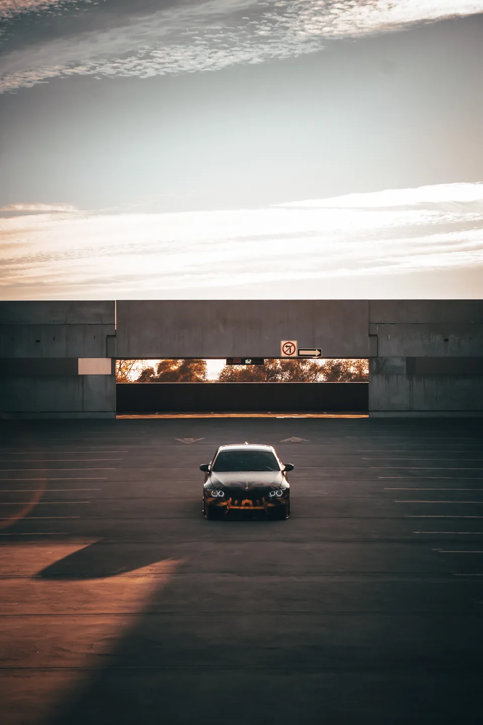 A car alone at the far end of an empty parking deck, sun flaring across the concrete.