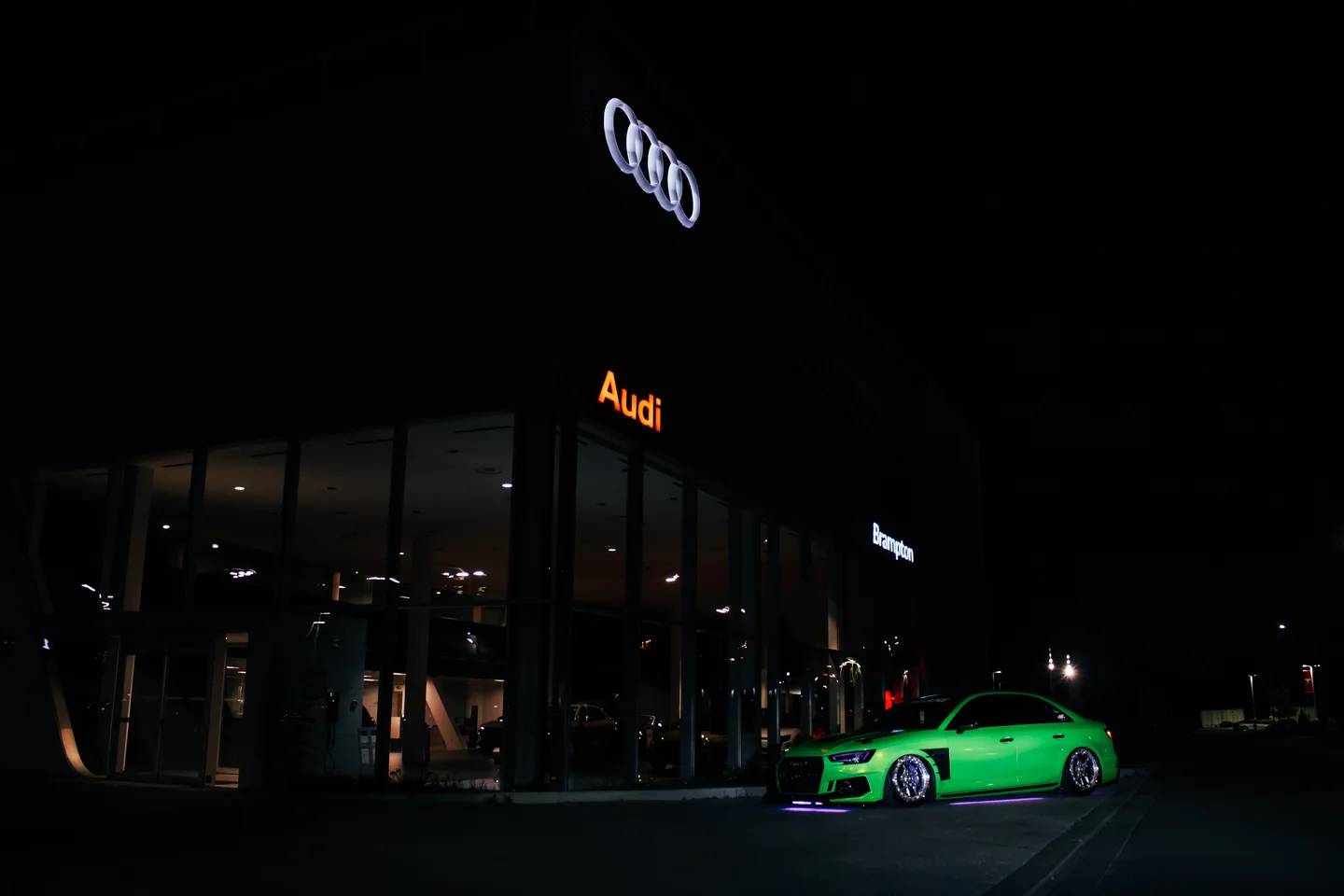 A green Audi S4 lit by its own underglow outside a closed Audi dealership at night.