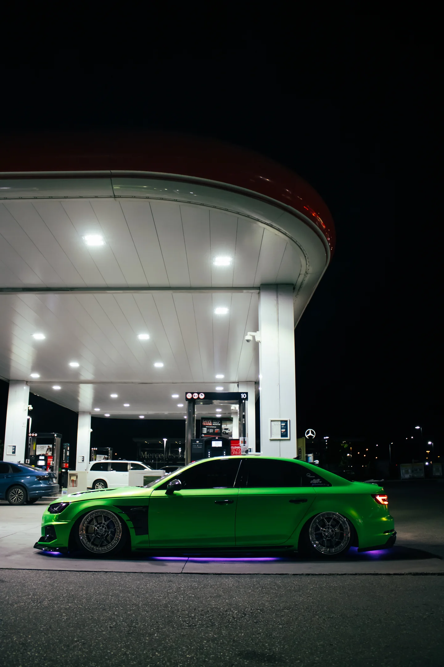 A green Audi S4 side-on under the hard white light of a gas station canopy.