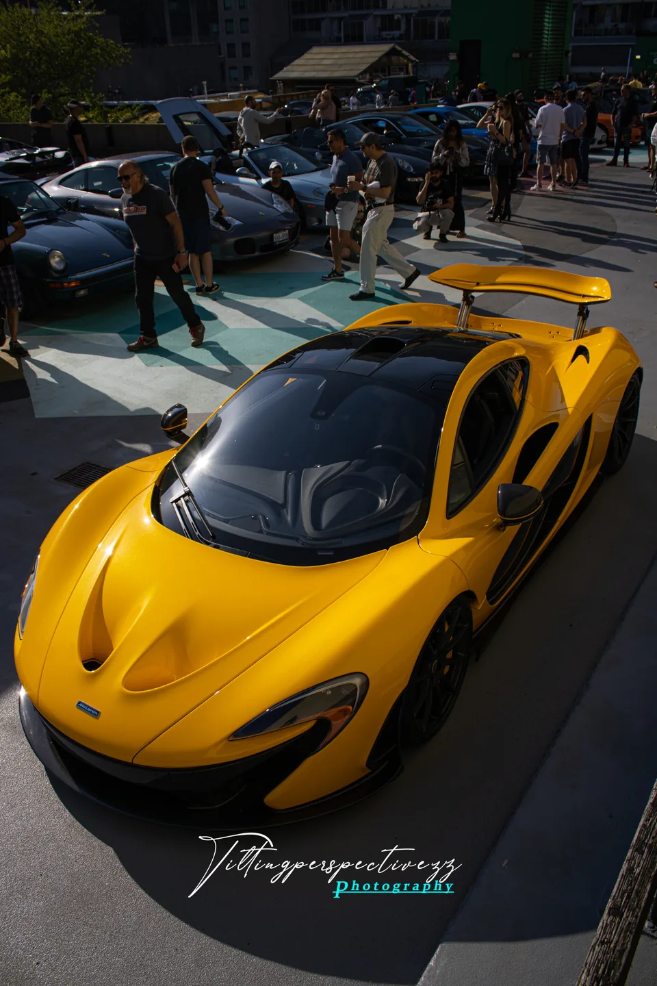 A yellow McLaren P1 parked among a crowd at a car meet.