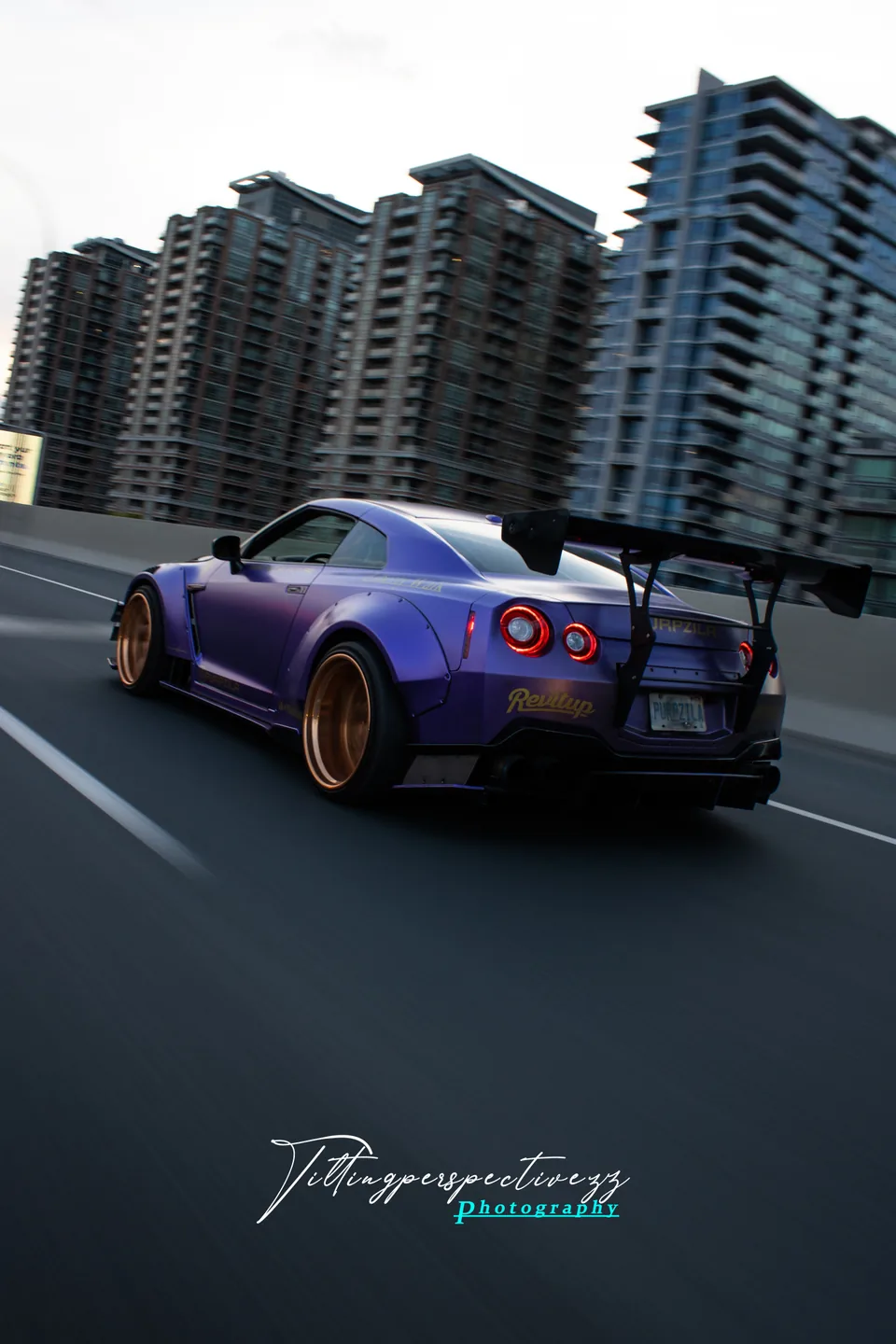 A purple Nissan GT-R in a rolling shot with the city rising behind it.