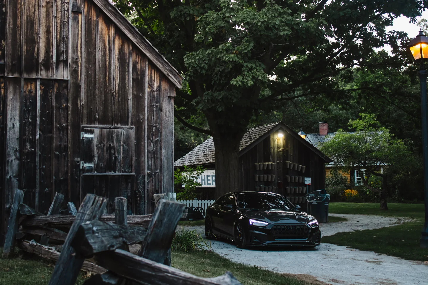 A black Audi S5 beside a weathered timber barn in low evening light.