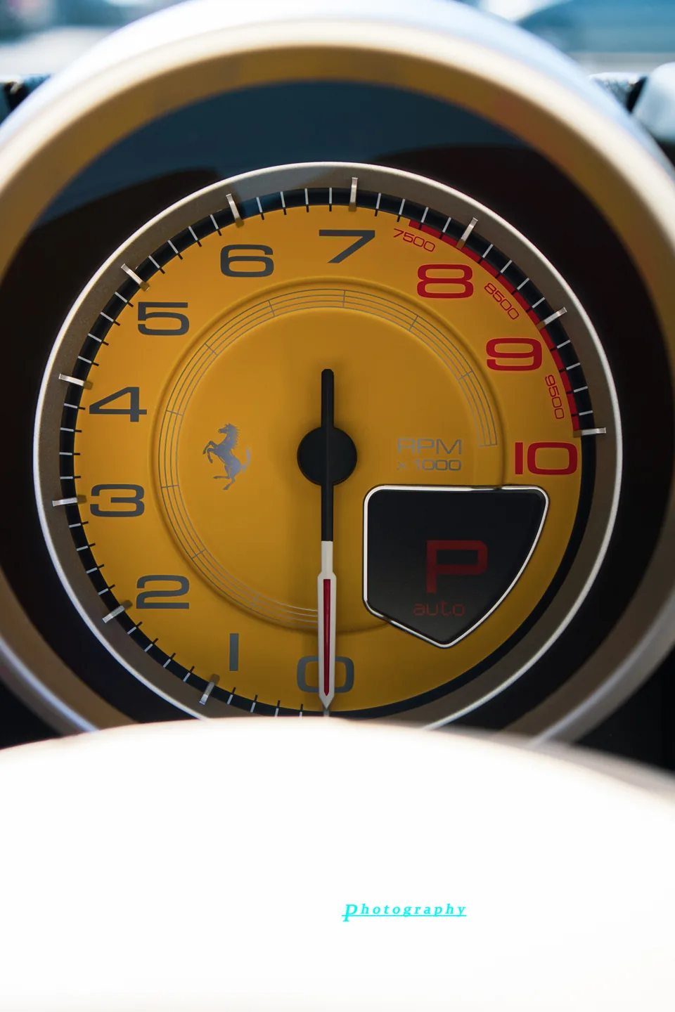Close detail of a Ferrari tachometer, yellow face and red numerals.