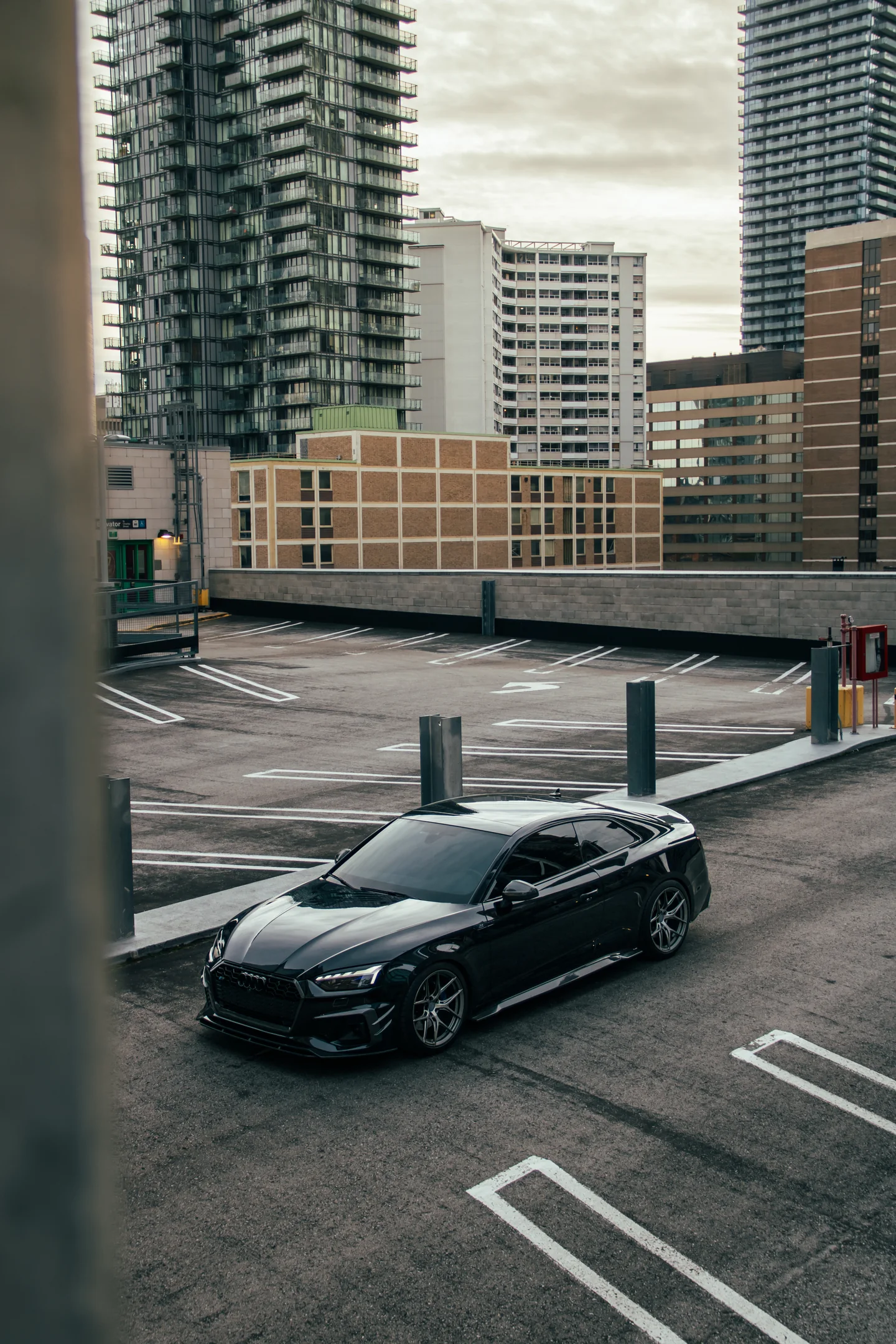 A black Audi S5 alone on an open parking deck above the Toronto condo skyline.