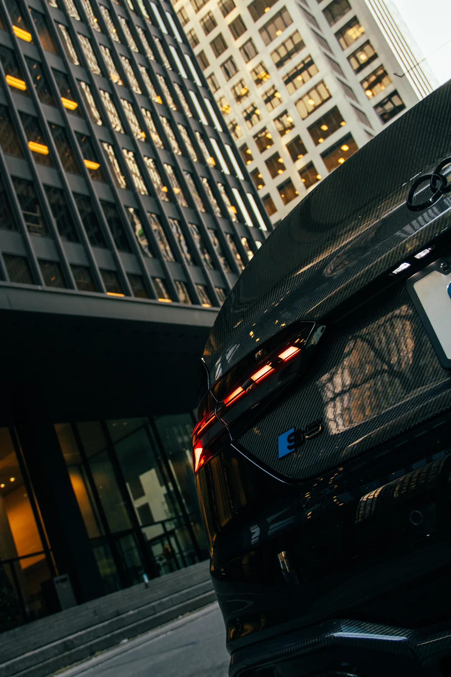 Low, tilted view along the front of a black Audi S5 with downtown Toronto towers rising behind it.
