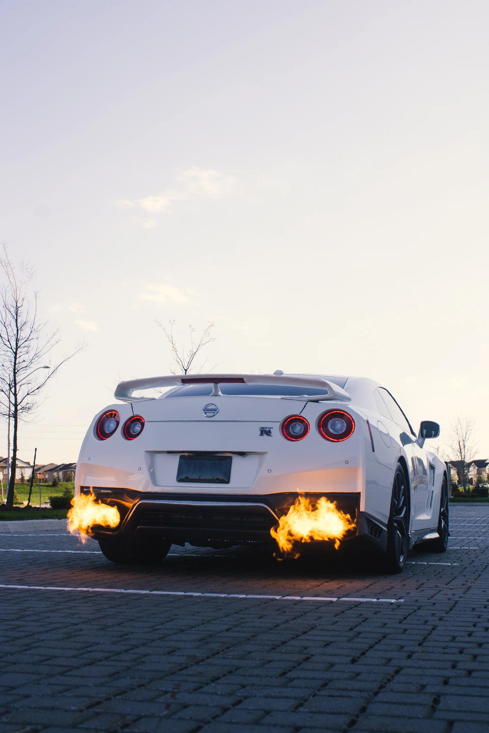 Rear view of a white Nissan GT-R with flame coming from both exhausts on brick pavers.