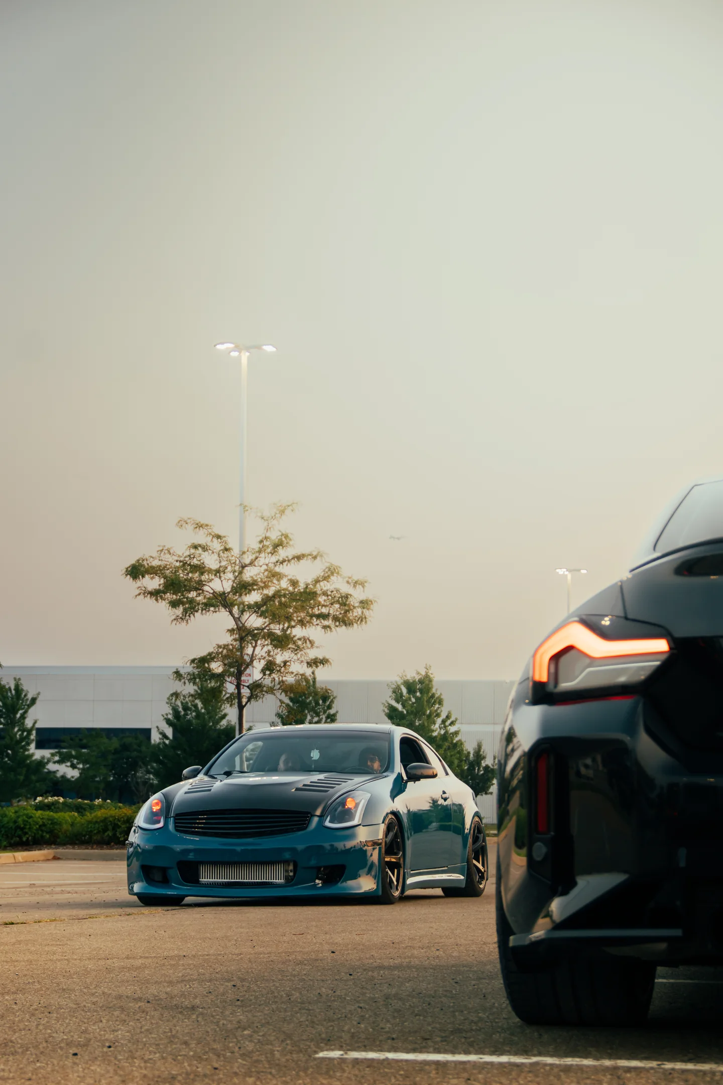 A white car and a black car at dusk with lake and streetlight behind them.