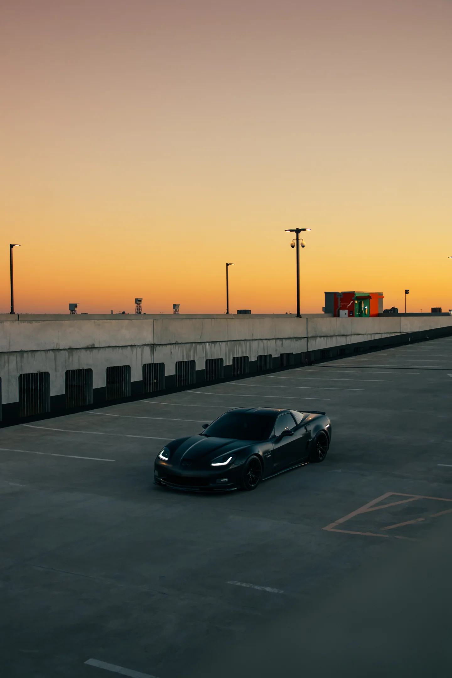 A black Corvette Z06 alone on an open parking deck as the sky turns orange behind it.