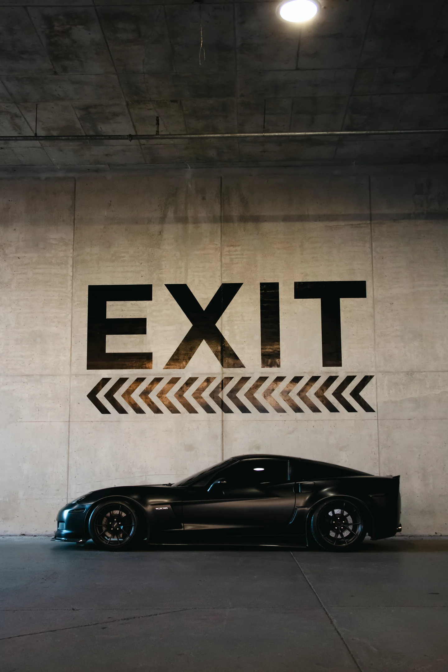 A black Corvette Z06 in profile beneath a concrete wall stencilled EXIT.